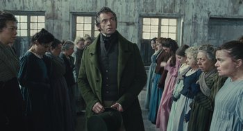 Movie still from “Les Misérables” (2012), directed by Tom Hooper – A group of people standing in a room with a man in a green coat; Medium shot, Low angle
