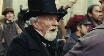 Movie still from “Les Misérables” (2012), directed by Tom Hooper – An old man with a beard wearing a top hat; Close Up shot, Over the shoulder angle