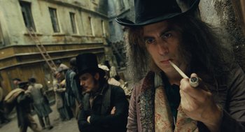 Movie still from “Les Misérables” (2012), directed by Tom Hooper – A man in a top hat smoking a cigarette in front of a crowd of people; Close Up shot, Over the shoulder angle