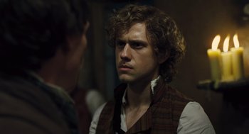 Movie still from “Les Misérables” (2012), directed by Tom Hooper – A man with curly brown hair and a brown vest; Close Up shot, Over the shoulder angle