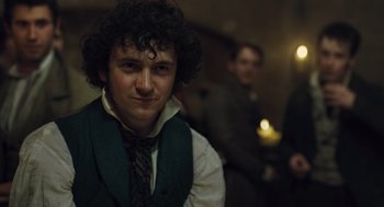 Movie still from “Les Misérables” (2012), directed by Tom Hooper – A man with curly hair wearing a green vest and a tie; Close Up shot, Over the shoulder angle