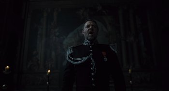 Movie still from “Les Misérables” (2012), directed by Tom Hooper – A man in a black military uniform standing in front of a wall; Medium shot, Low angle