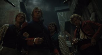Movie still from “Les Misérables” (2012), directed by Tom Hooper – A group of people standing around in a dark room; Medium shot, Low angle