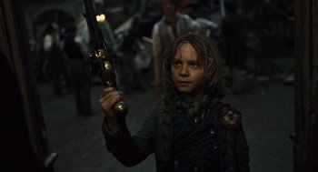 Movie still from “Les Misérables” (2012), directed by Tom Hooper – A young boy holding a rifle in a crowd; Medium shot, Low angle
