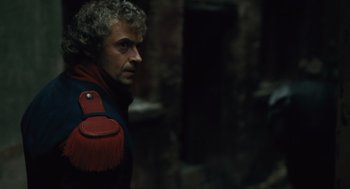 Movie still from “Les Misérables” (2012), directed by Tom Hooper – A man in a red and black jacket standing next to a brick wall; Close Up shot, Over the shoulder angle