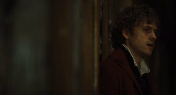 Movie still from “Les Misérables” (2012), directed by Tom Hooper – A man with curly hair wearing a red coat; Close Up shot, Over the shoulder angle