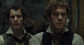 Movie still from “Les Misérables” (2012), directed by Tom Hooper – Two men standing next to each other in front of a wall; Close Up shot, Over the shoulder angle