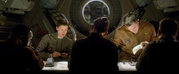 Movie still from “Life” (2017), directed by Daniel Espinosa – A group of people sitting around a table; Medium shot, Over the shoulder angle