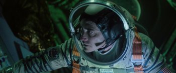 Movie still from “Life” (2017), directed by Daniel Espinosa – A man in a spacesuit is looking into a mirror; Medium shot, Overhead angle