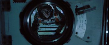 Movie still from “Life” (2017), directed by Daniel Espinosa – A man in a space suit looking at himself in a mirror; Medium shot, Low angle