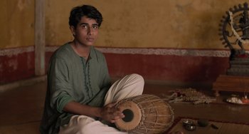 Movie still from “Life of Pi” (2012), directed by Ang Lee – A man sitting on the ground holding a drum; Medium shot, Low angle