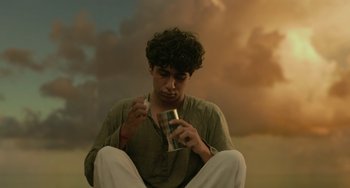 Movie still from “Life of Pi” (2012), directed by Ang Lee – A man sitting on the ground with a can in his hand; Medium shot, Low angle