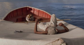 Movie still from “Life of Pi” (2012), directed by Ang Lee – A man laying on the back of a boat next to a tiger; Wide shot, Low angle