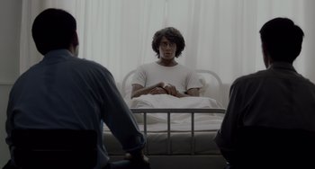 Movie still from “Life of Pi” (2012), directed by Ang Lee – A man sitting in a bed in front of two other men; Medium shot, Over the shoulder angle