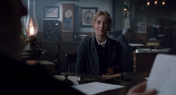 Movie still from “Little Women” (2019), directed by Greta Gerwig – A woman sitting at a table in front of papers; Medium shot, Over the shoulder angle