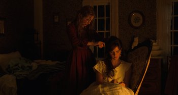 Movie still from “Little Women” (2019), directed by Greta Gerwig – Two women in a dark room one is cutting the hair of the other; Medium shot, High angle