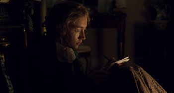 Movie still from “Little Women” (2019), directed by Greta Gerwig – A person sitting in the dark looking at a book; Close Up shot, Over the shoulder angle