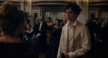 Movie still from “Little Women” (2019), directed by Greta Gerwig – A man in a white shirt and a tie standing in front of a group of people; Medium shot, Over the shoulder angle