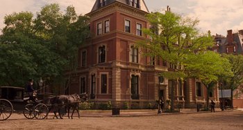 Movie still from “Little Women” (2019), directed by Greta Gerwig – Two horses pulling a carriage down the street in front of a large brick building; Extreme Wide shot, Low angle