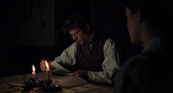 Movie still from “Little Women” (2019), directed by Greta Gerwig – A man sitting at a table reading a book; Medium shot, Over the shoulder angle