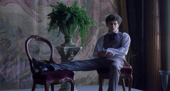 Movie still from “Little Women” (2019), directed by Greta Gerwig – A young man sitting on a chair next to a potted plant; Medium shot, Low angle