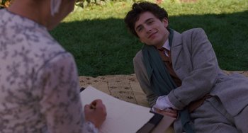 Movie still from “Little Women” (2019), directed by Greta Gerwig – A young man sitting on the ground while holding a sheet of paper; Medium shot, Over the shoulder angle