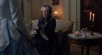 Movie still from “Little Women” (2019), directed by Greta Gerwig – An older woman sitting on a couch in a room; Medium shot, Over the shoulder angle