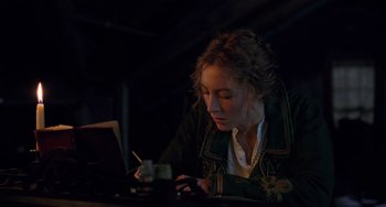 Movie still from “Little Women” (2019), directed by Greta Gerwig – A woman sitting at a table looking at a laptop computer; Medium shot, High angle