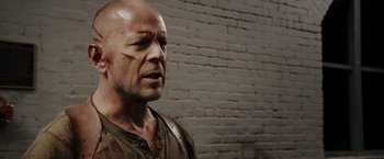 Movie still from “Live Free or Die Hard” (2007), directed by Len Wiseman – A man with a scar on his face is standing in front of a brick wall; Close Up shot, Over the shoulder angle
