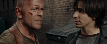 Movie still from “Live Free or Die Hard” (2007), directed by Len Wiseman – A man and a woman standing next to each other in front of a brick wall; Close Up shot, Over the shoulder angle