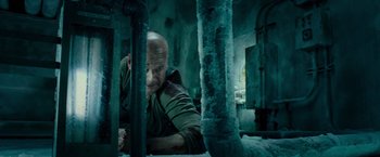 Movie still from “Live Free or Die Hard” (2007), directed by Len Wiseman – A bald man in a green shirt is leaning against a wall; Medium shot, Low angle