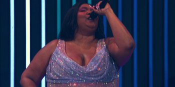 Movie still from “Lizzo: Live in Concert” (2022), directed by Brad Duns – A woman in a silver dress singing into a microphone; Medium shot, Low angle