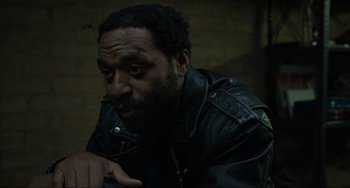 Movie still from “Locked Down” (2021), directed by Doug Liman – A man in a black leather jacket sitting in front of a brick wall; Close Up shot, High angle