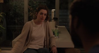 Movie still from “Locked Down” (2021), directed by Doug Liman – A woman sitting at a table with a drink in front of her; Medium shot, Over the shoulder angle