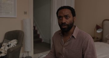 Movie still from “Locked Down” (2021), directed by Doug Liman – A man in a brown shirt is standing in a room; Close Up shot, Over the shoulder angle