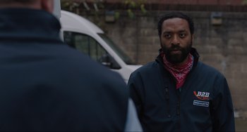 Movie still from “Locked Down” (2021), directed by Doug Liman – A man in a black jacket standing next to a white van; Medium shot, Over the shoulder angle