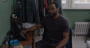 Movie still from “Locked Down” (2021), directed by Doug Liman – A man sitting at a table in front of clothes; Medium shot, High angle