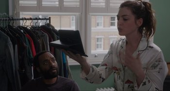 Movie still from “Locked Down” (2021), directed by Doug Liman – A woman showing a man a book in front of a window; Medium shot, Over the shoulder angle