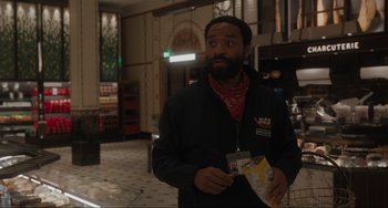 Movie still from “Locked Down” (2021), directed by Doug Liman – A man in a black jacket is holding some food; Medium shot, Over the shoulder angle