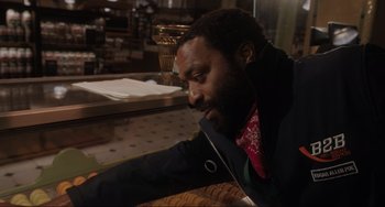 Movie still from “Locked Down” (2021), directed by Doug Liman – A man sitting at a table in front of a counter; Close Up shot, Low angle