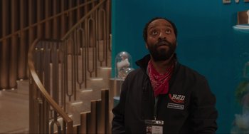 Movie still from “Locked Down” (2021), directed by Doug Liman – A man in a black jacket and red bandanna looking up; Medium shot, Over the shoulder angle