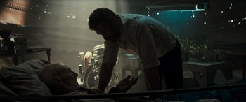 Movie still from “Logan” (2017), directed by James Mangold – A man standing next to a table in a room; Medium shot, Over the shoulder angle