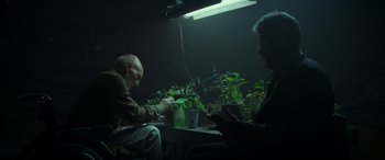 Movie still from “Logan” (2017), directed by James Mangold – Two people sitting in a dark room with plants; Medium shot, Low angle