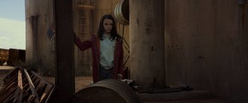 Movie still from “Logan” (2017), directed by James Mangold – A woman in a red jacket standing next to a barrel; Medium shot, Low angle