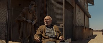 Movie still from “Logan” (2017), directed by James Mangold – An old man sitting in a chair with a mask on; Medium shot, Over the shoulder angle