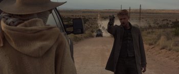 Movie still from “Logan” (2017), directed by James Mangold – A man holding up a gun while standing next to a car; Medium shot, Over the shoulder angle