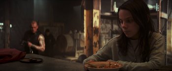 Movie still from “Logan” (2017), directed by James Mangold – A woman sitting at a table with a plate of food; Medium shot, Over the shoulder angle