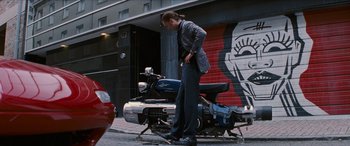 Movie still from “Looper” (2012), directed by Rian Johnson – A woman standing on a motorcycle on the side of the street; Wide shot, Low angle