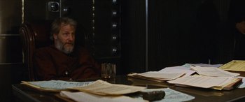 Movie still from “Looper” (2012), directed by Rian Johnson – An older man sitting at a table with papers and a glass; Medium shot, Over the shoulder angle