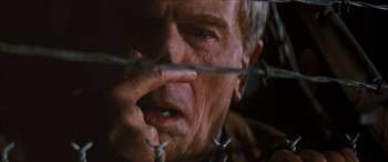 Movie still from “Looper” (2012), directed by Rian Johnson – An older man is looking through barbed wire; Extreme Close Up shot, Low angle